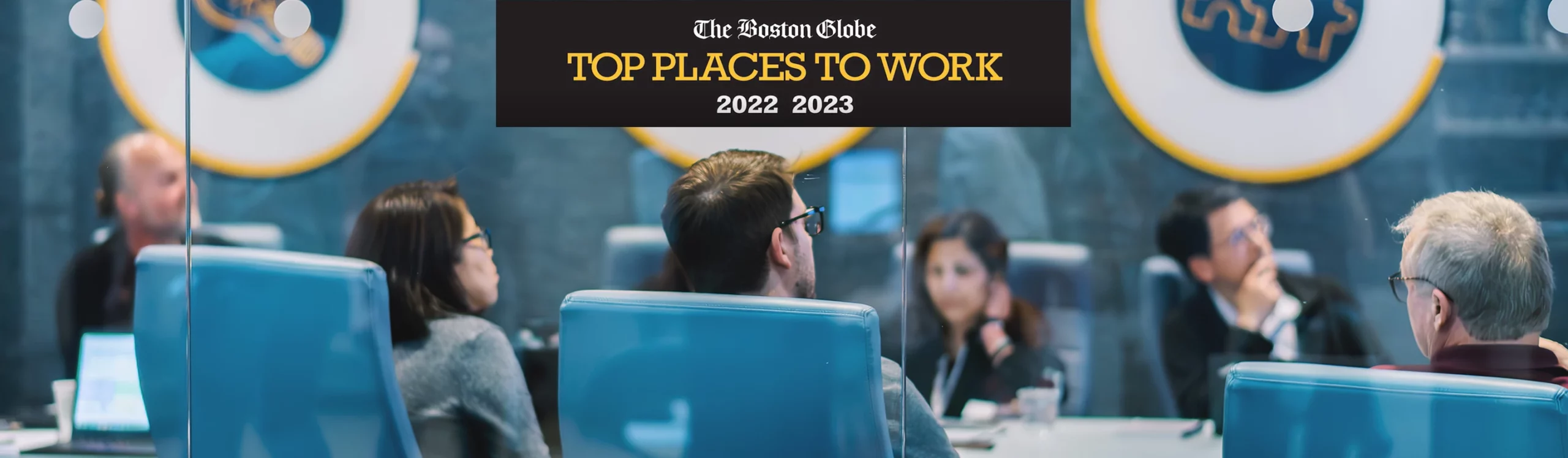 Kymera employees in a meeting room with “The Boston Globe TOP PLACES TO WORK 2022 2023” banner above